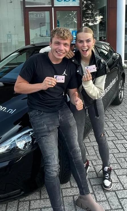 Twee blije geslaagde leerlingen tonen trots hun behaalde rijbewijs bij de lesauto voor het CBR.