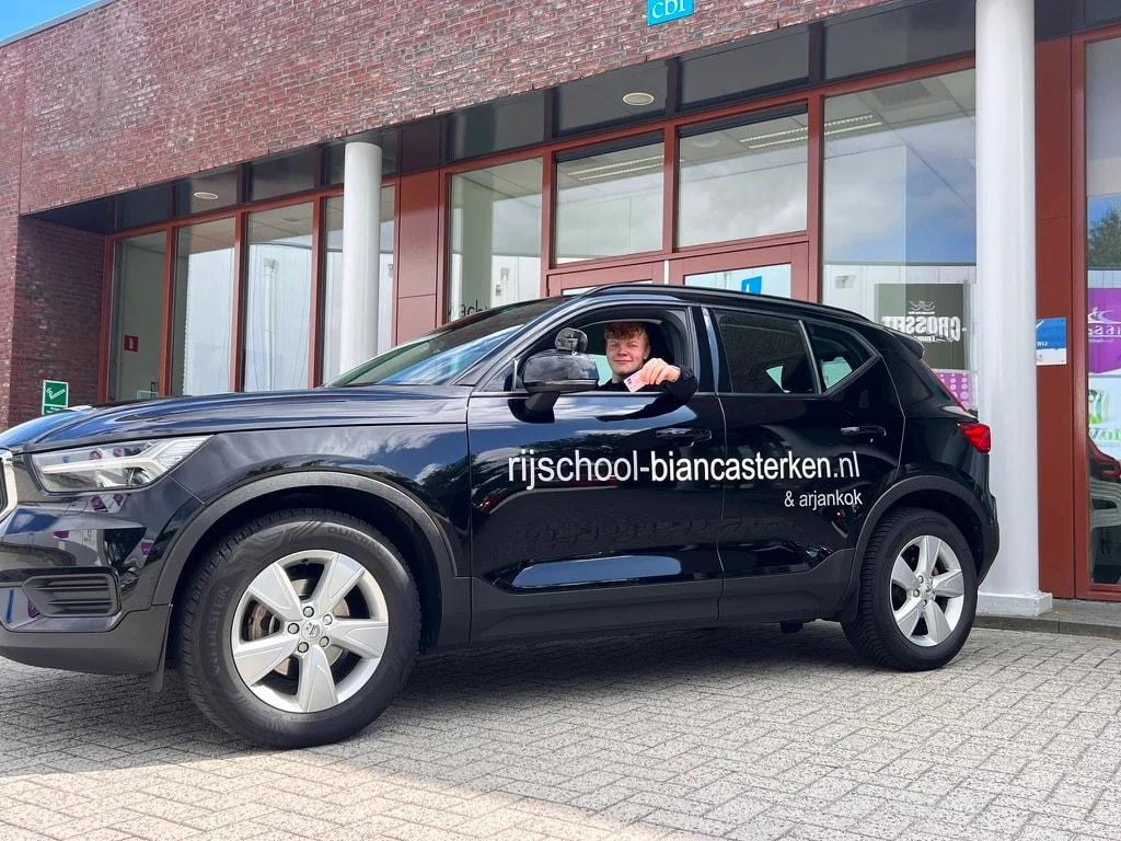 Rijinstructrice Bianca Sterken trots poserend bij haar moderne Volvo lesauto.