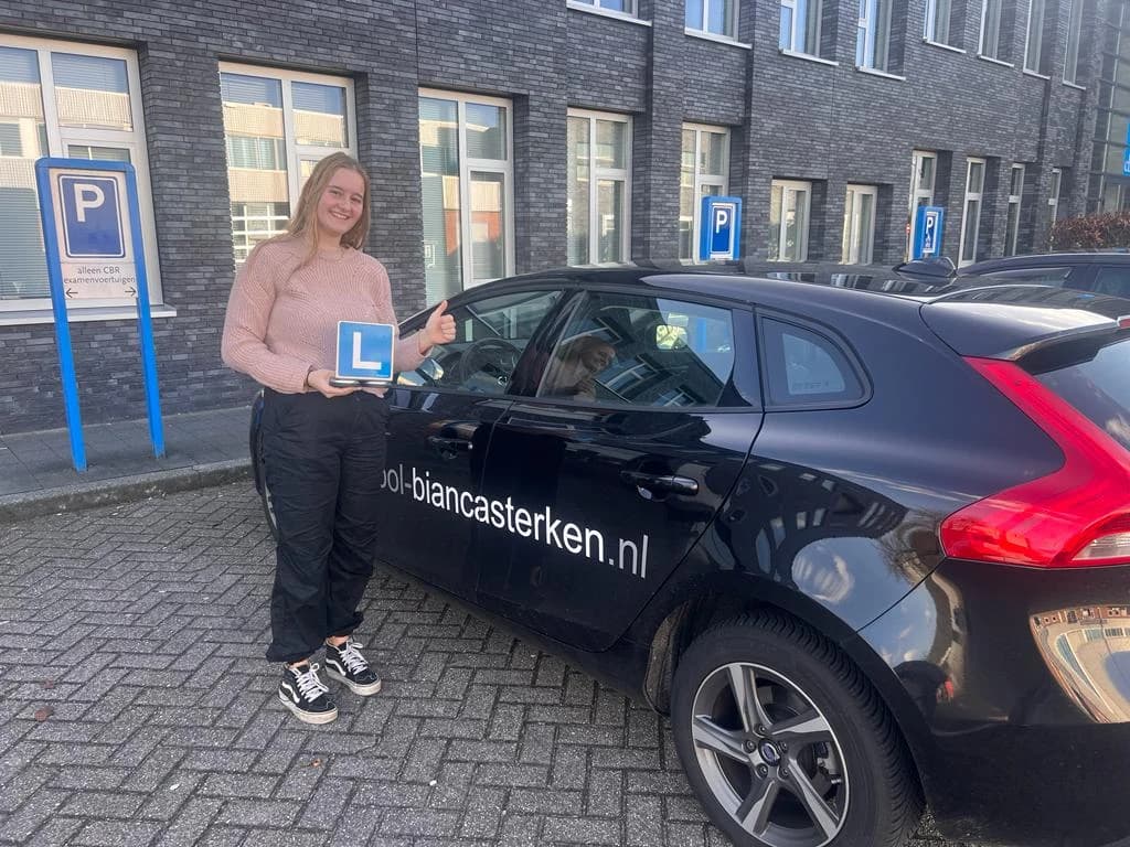 Geslaagde leerling met L-bordje en duim omhoog bij de lesauto voor het CBR examencentrum in Zwolle.
