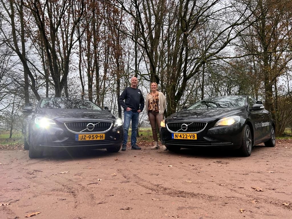 Rijinstructeurs Arjan Kok en Bianca Sterken tussen de twee lesauto's met brandende koplampen.