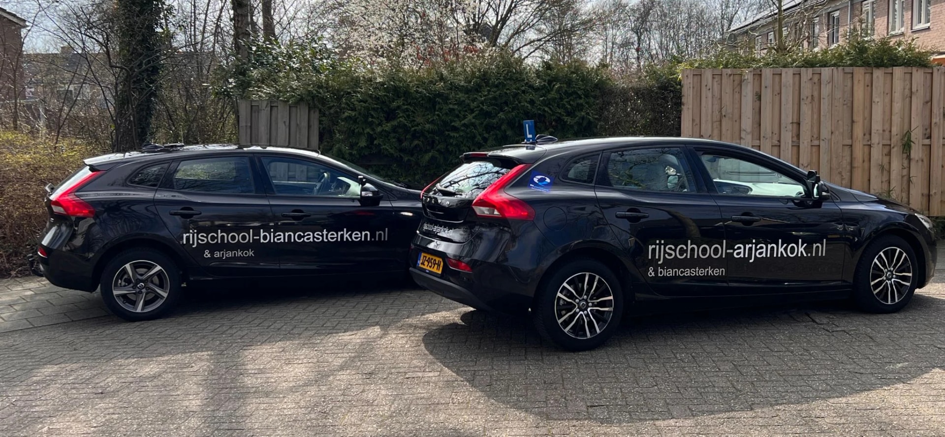Panoramische weergave van de twee zwarte Volvo lesauto's op de oprit.