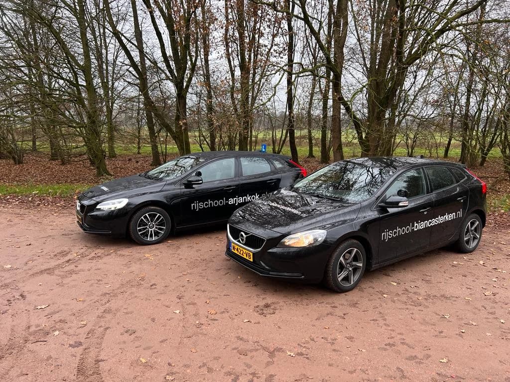 Twee zwarte Volvo lesauto's geparkeerd op een bospad in het bos.